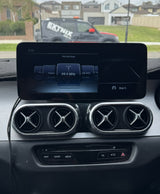 Merc Xclass w205 dashboard with a navigation screen displaying a radio station, with a vehicle and house in the background.
